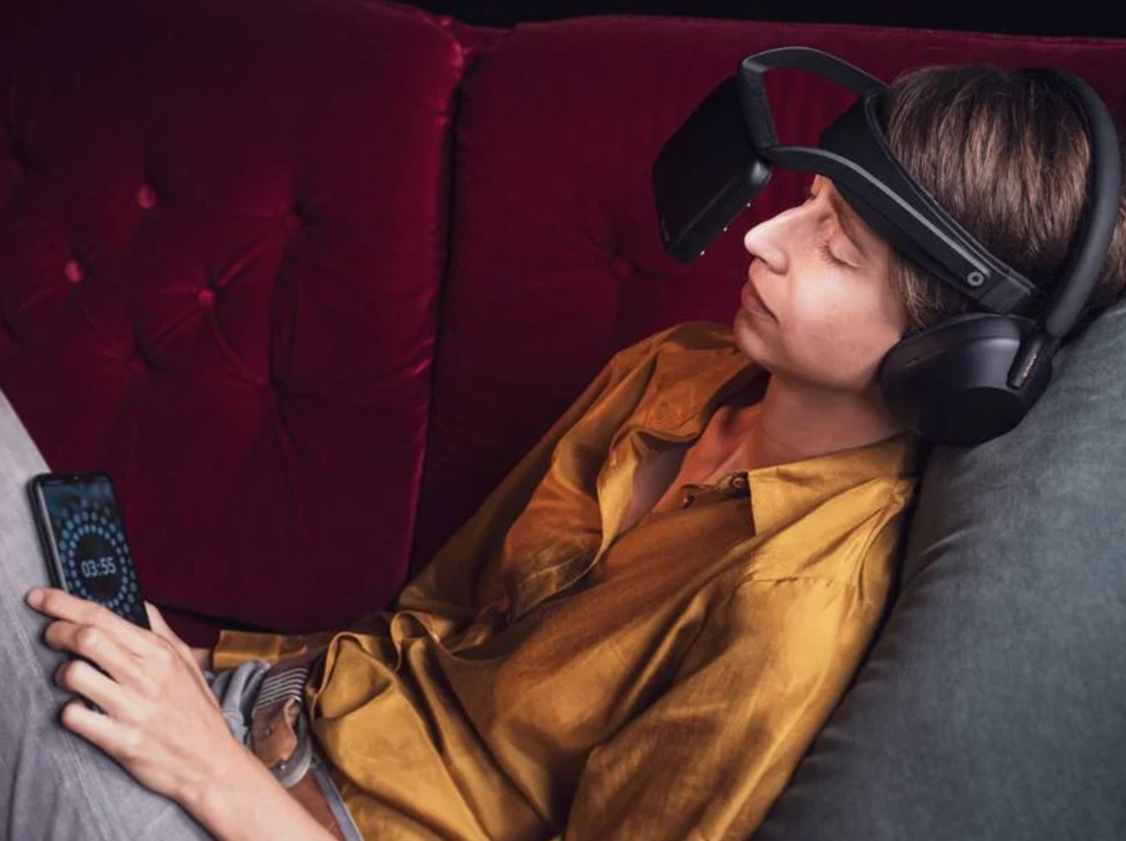 A person reclining in a red chair wearing the NeuroVIZR and checking the app
